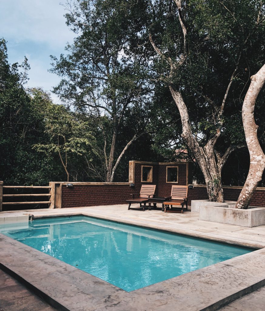 piscine avec margelles effet beton et deux transats en bois sous des arbres